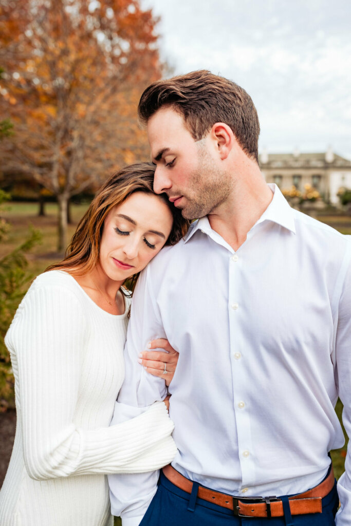 Sensual and affectionate moment is captured as the woman closes her eyes, embracing the man's arm while leaning her head on his shoulder. Simultaneously, the man leans his head on the woman's, creating a tender connection between them.
