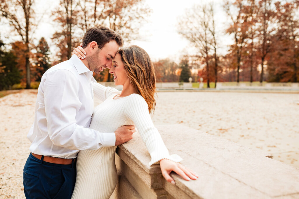 Tender moment frozen in time, with a man holding the woman's back as they lean their heads on each other, both sharing heartfelt smiles. The woman's back rests against the concrete, creating a serene and intimate atmosphere.