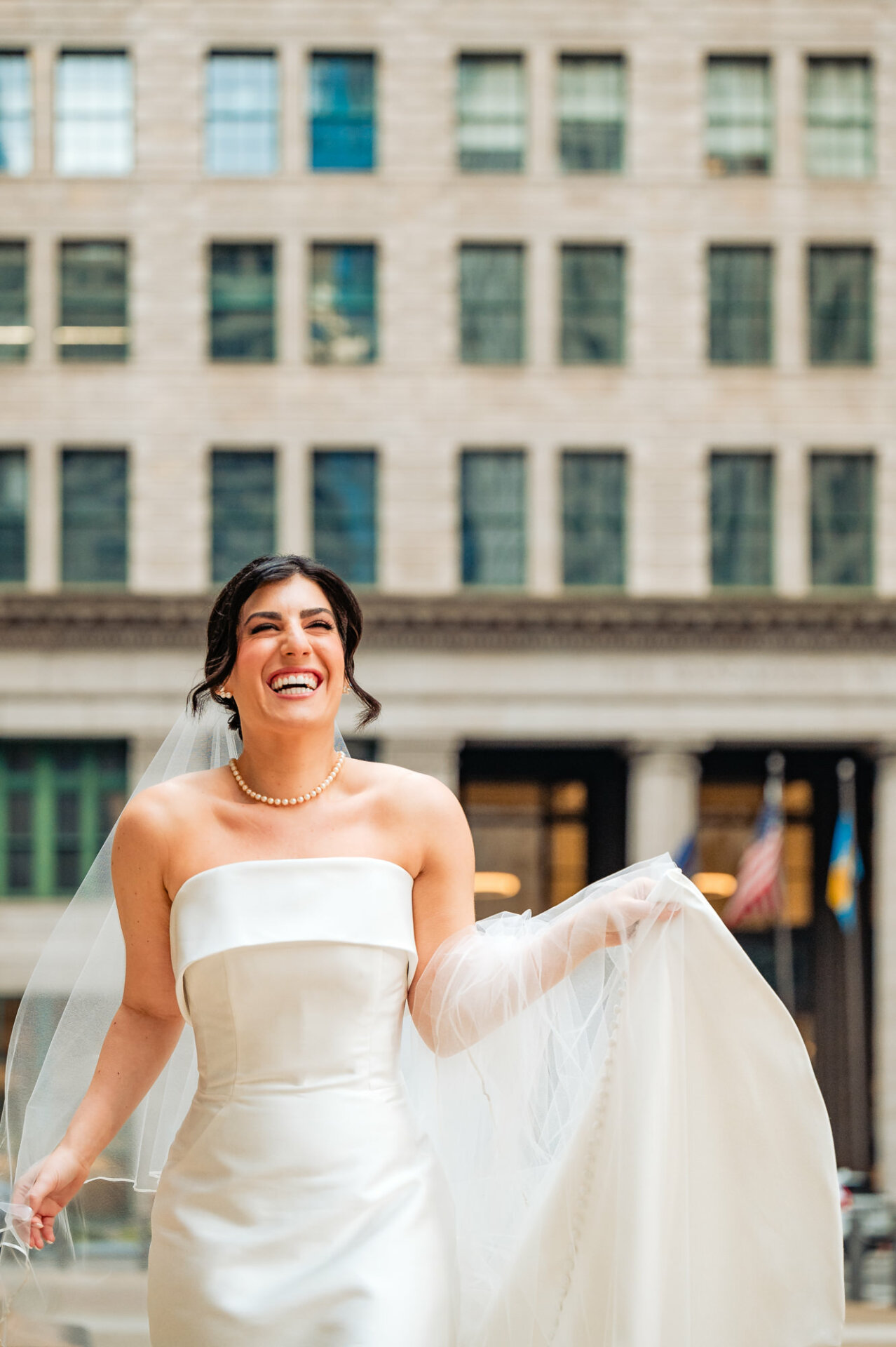 The bride's radiant smile lights up the frame as she delicately holds her veil, her eyes sparkling with joy and anticipation on this momentous day of her wedding.