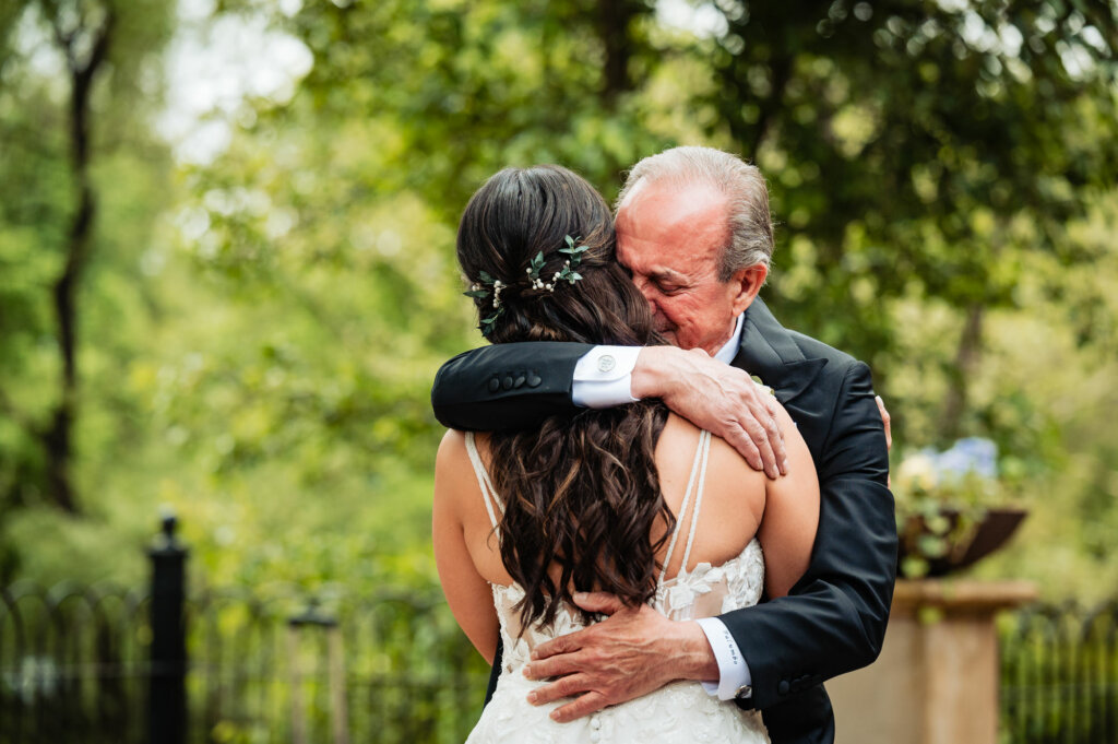 The bride is enveloped in a warm embrace by her father after their first look, a poignant moment filled with love and pride as they share in the emotion of this special day.