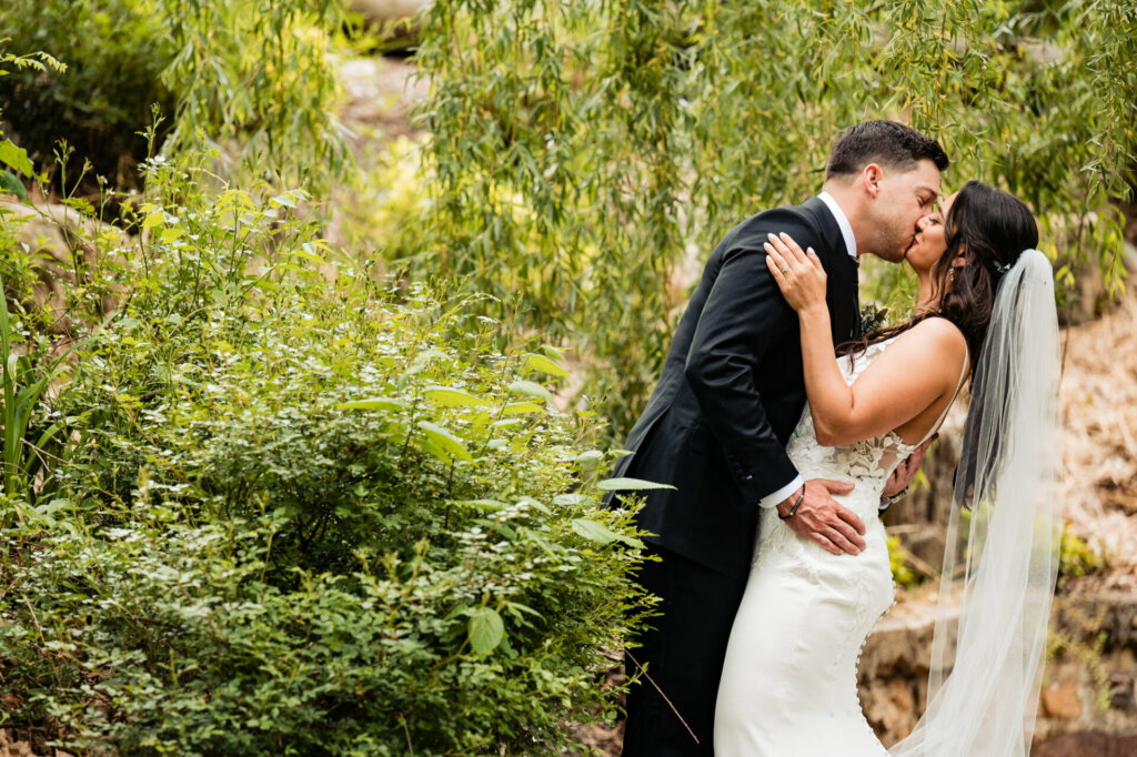 The groom and his bride share a tender kiss amidst the enchanting beauty of the garden