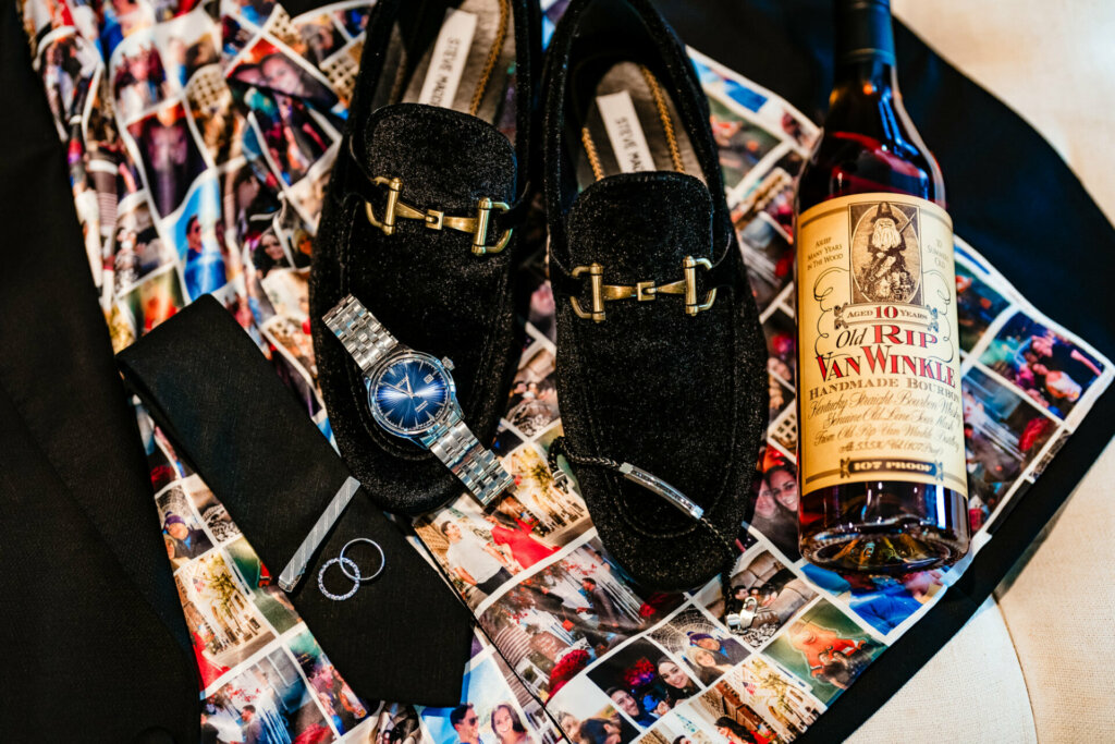 Arranged artfully together for a wedding still life are essential accessories atop a jacket liner comprised of photo collages of the bride and groom together. Laid out neatly are the groom’s polished leather shoes, an intricate boutinnniere, a half-filled crystal whiskey glass, his engraved watch and bowtie. These items rest on a paisley print lining from the groom’s tailored tuxedo jacket, the innermost layer underneath - mimicking how partnerships grow from sequential depths of intimacy.