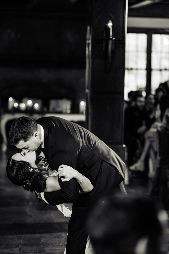 In a timeless black and white shot, the bride bends gracefully as she is kissed by her groom, their embrace captured in a moment of timeless elegance