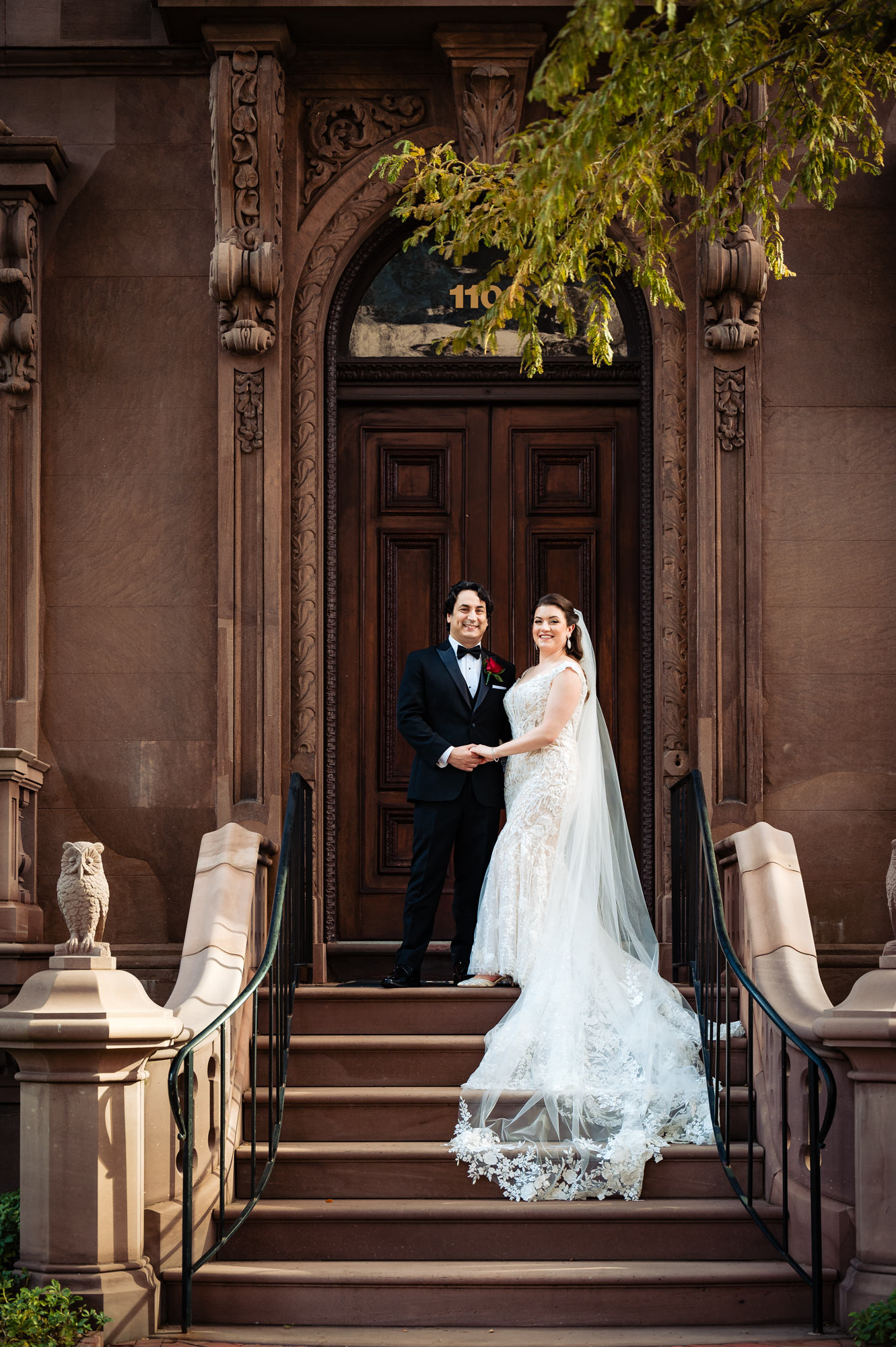 Bride and groom stand on stairs with a rustic wooden door backdrop in their wedding portrait.