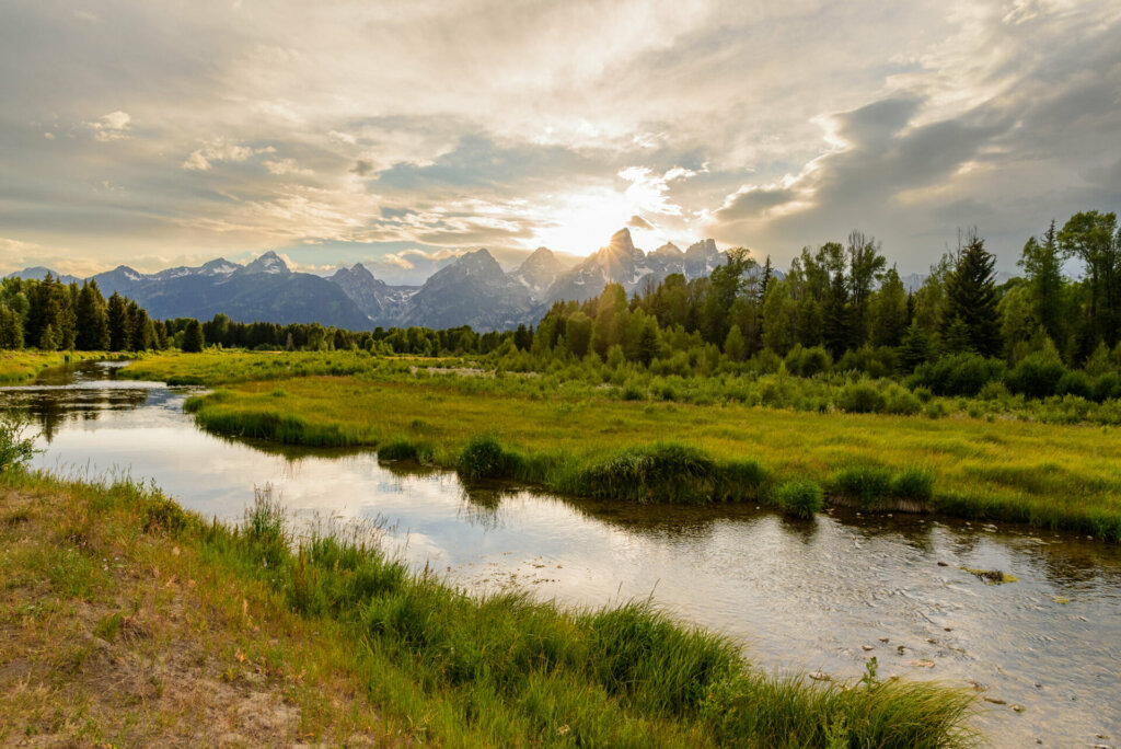A serene lake reflects the towering peaks of the Grand Tetons, its tranquil waters mirroring the majestic beauty of the surrounding mountains