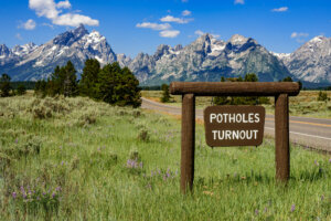 A roadside sign reads 'Potholes Turnout,' indicating a designated area for drivers to pull over and observe natural potholes formations, typical of the landscape in the area.
