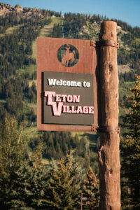 A signboard stands prominently, displaying the words 'Welcome to Teton Village,' greeting visitors to this scenic destination nestled amidst the majestic beauty of the Grand Tetons.