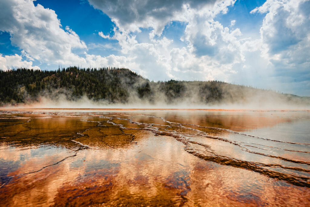The Old Faithful geyser basin at Yellowstone National Park, showcasing a landscape of colorful geothermal features, steam rising from various geysers and hot springs, surrounded by the natural beauty of the park's wilderness