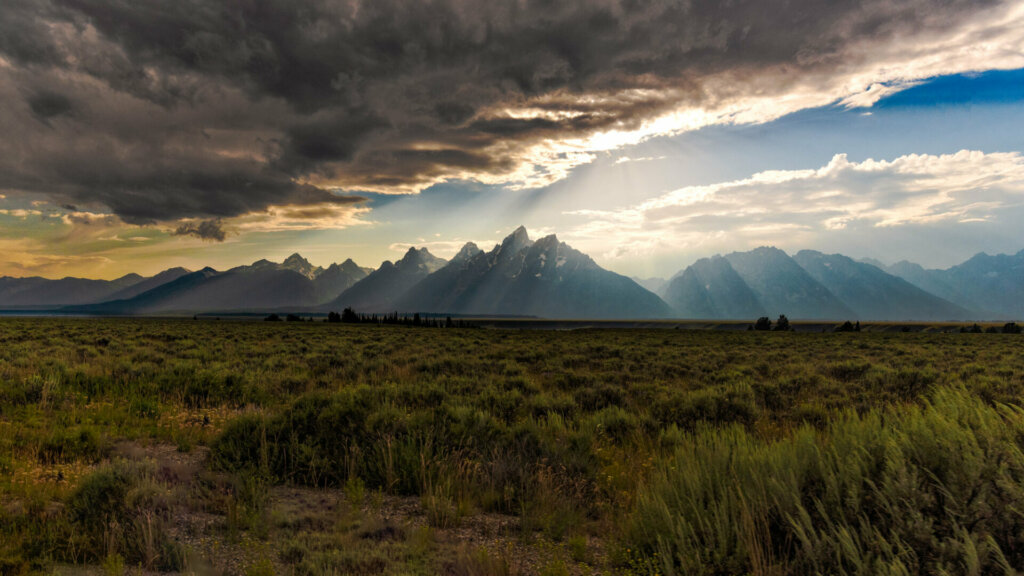 The majestic Tetons rise in the distance, as seen from outside of Brigg's, Idaho, offering a breathtaking view of the iconic mountain range against the vast expanse of the Idaho landscape.
