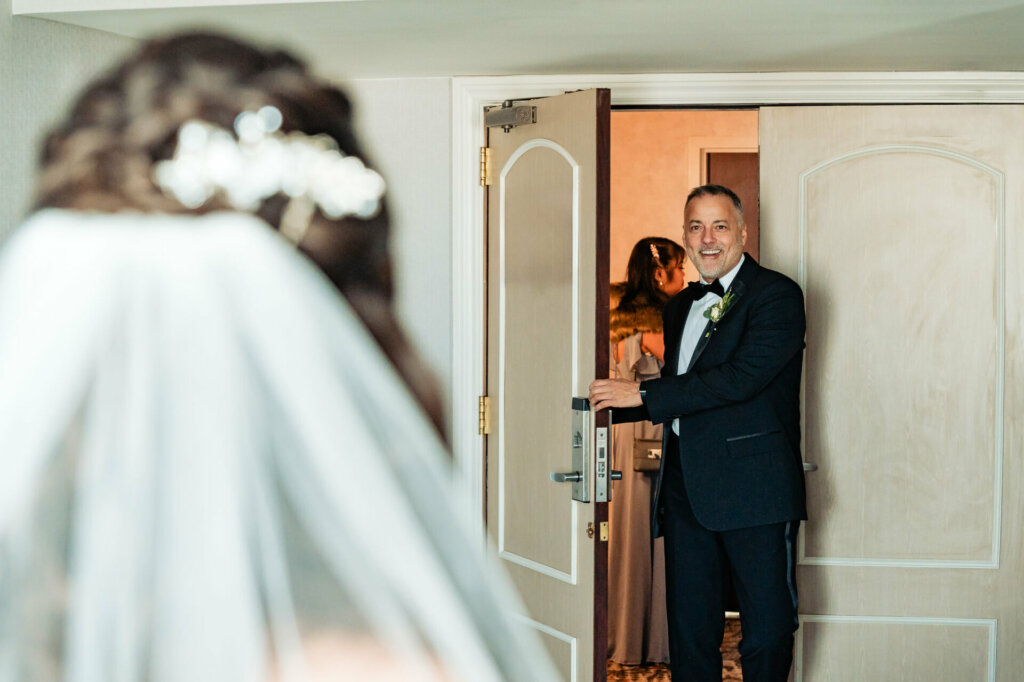 The bride's father stands in awe, his eyes filled with emotion, as he sees his daughter for the first time on her wedding day