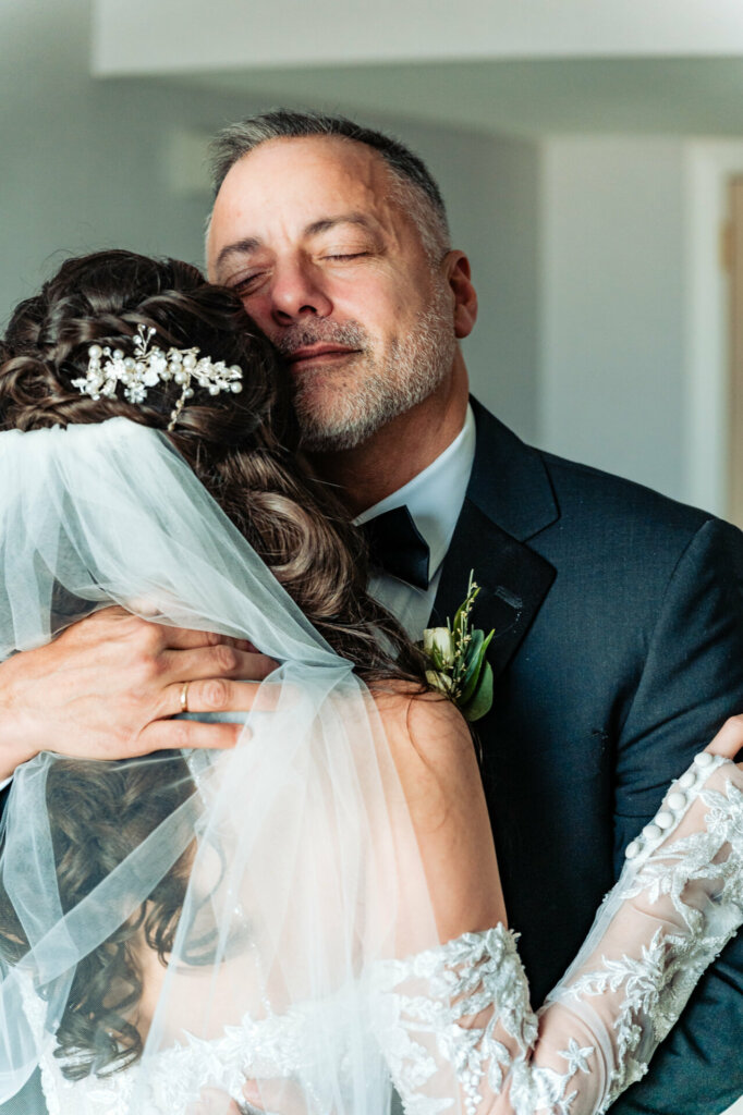 The bride's father wraps his arms around her in a warm embrace after their first look, sharing a tender moment filled with love, pride, and anticipation