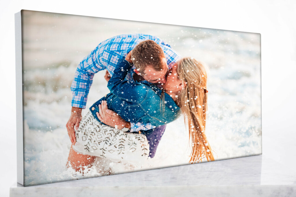 A romantic wall art depicting a couple passionately kissing on a sandy beach shore. The gentle waves lap at the shore as the couple embraces in a moment of joy and commitment
