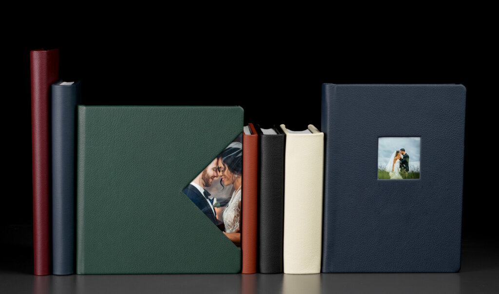 A row of colorful wedding albums with a variety of designs. The albums boast different cover materials like leather, fabric, and wood, with some featuring photo displays and others showcasing minimal text. Frame colors also range from classic to modern