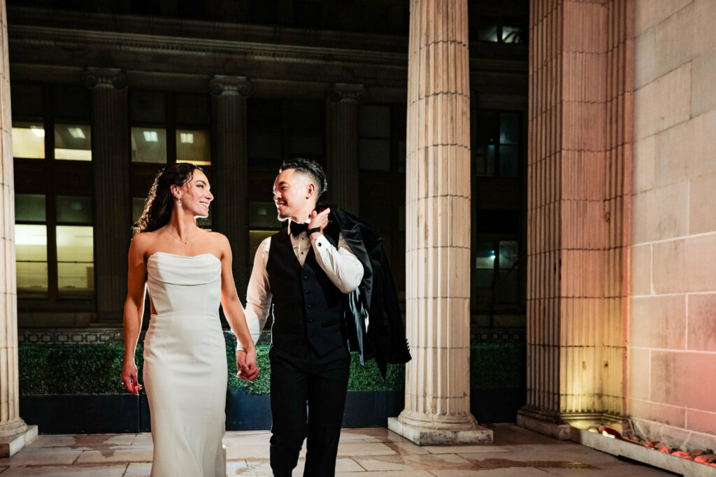 Sporting casual attire and sneakers, the newlywed couple walks hand in hand, exchanging affectionate glances, their radiant smiles reflecting the joy of beginning their married life together.
