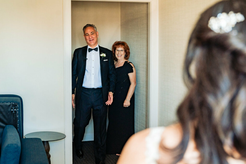 Proud parents of the bride smiling with joy upon their first glimpse of their daughter in her wedding attire.