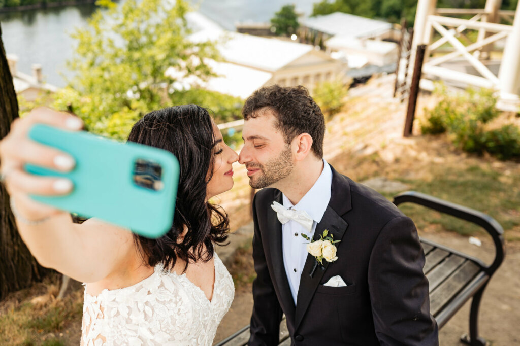 Bride holding up her phone to capture a selfie as the couple leans in for a kiss shot