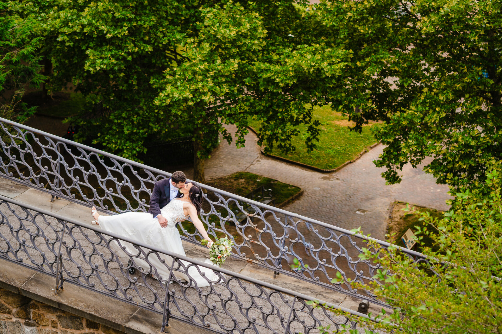 Newlyweds, bathed in timeless elegance, pause for a portrait beside an ornate iron railing