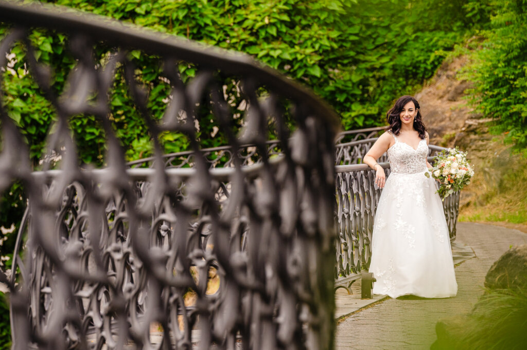 Elegant bride, in a flowing gown, pauses for a timeless portrait beside an ornate iron railing.