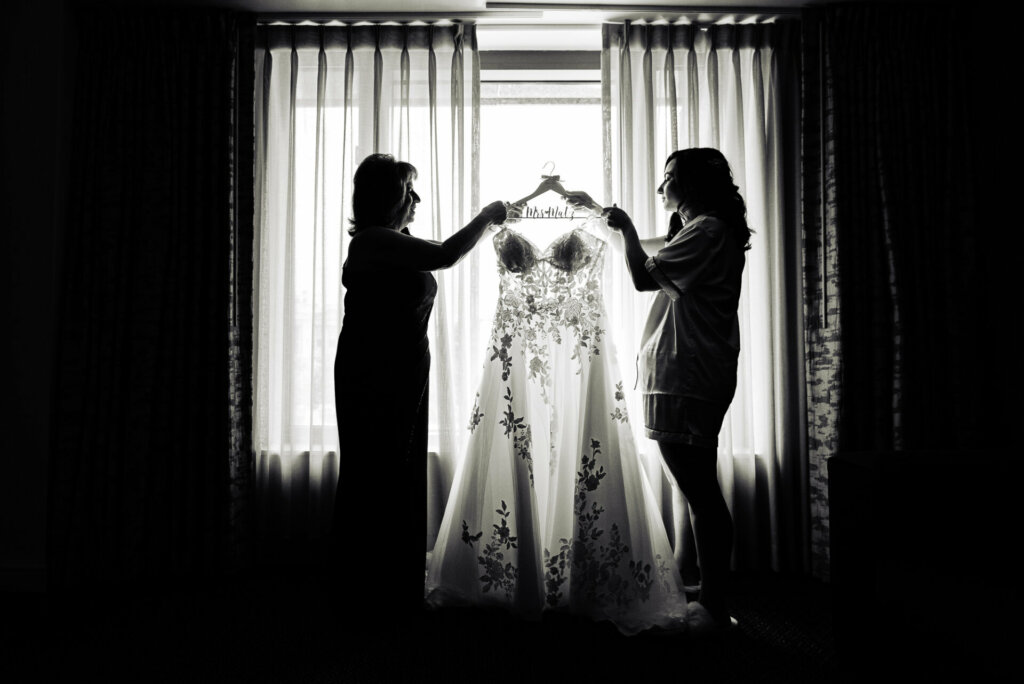 Silhouette shot of black and white image of bride and her mother holding up the wedding gown together.