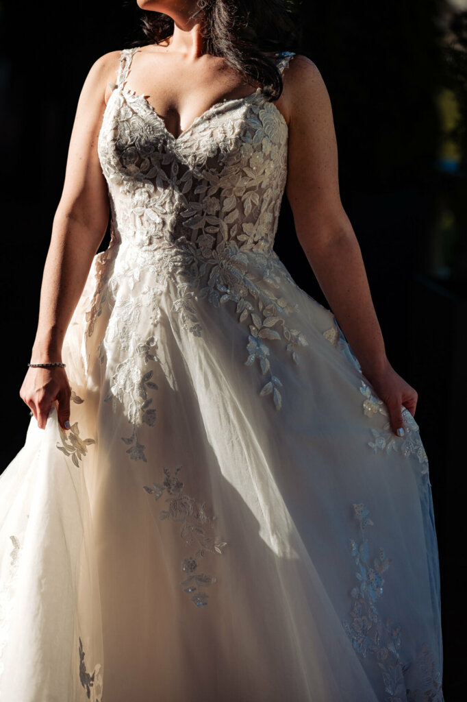 Bride illuminated by warm, golden light as she gracefully holds her wedding gown.