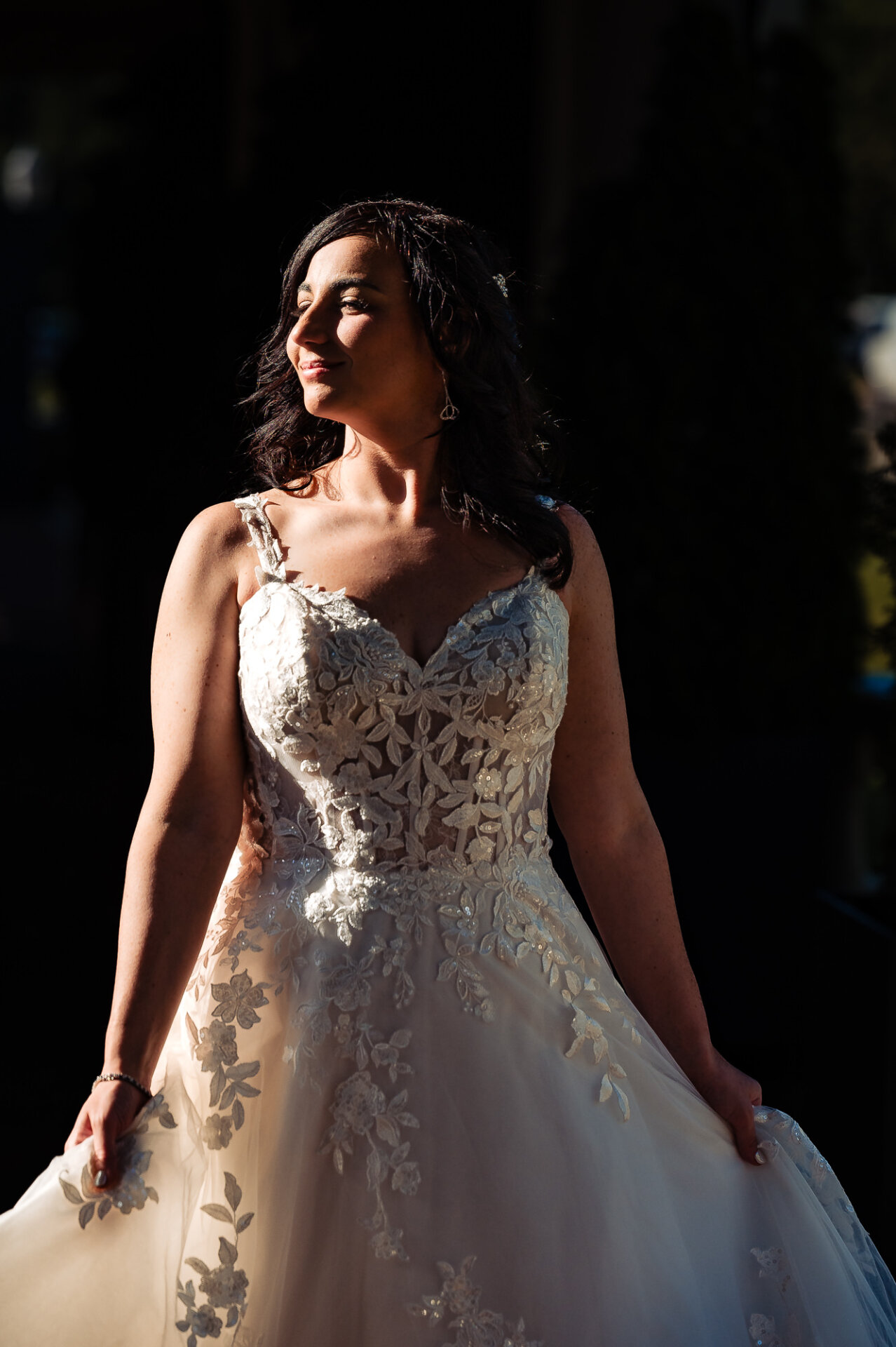 Radiant bride smiling warmly, bathed in soft light, as she holds her wedding gown.