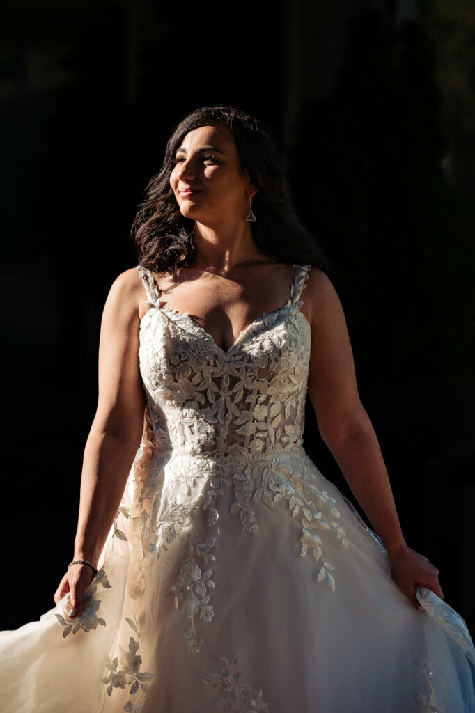 Radiant bride smiling warmly, bathed in soft light, as she holds her wedding gown.