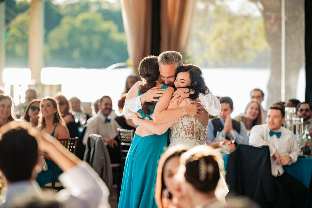 Emotional moment as the bride's father embraces both his daughter and wife during their dance at the wedding reception.