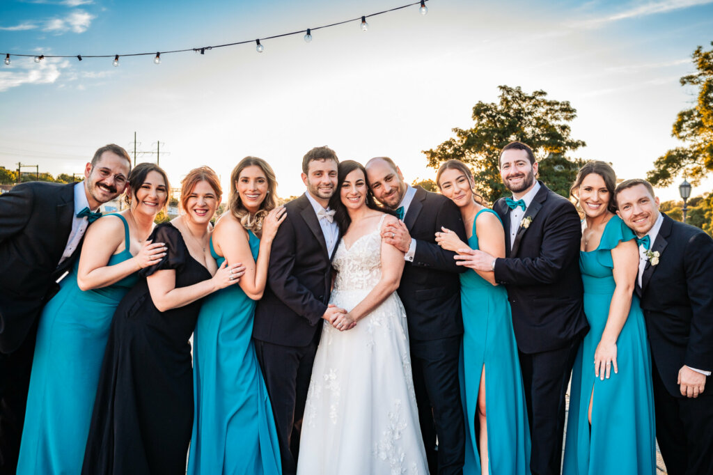 Elegant newlyweds celebrate their union with their radiant bridal party on a picturesque lakeside terrace.