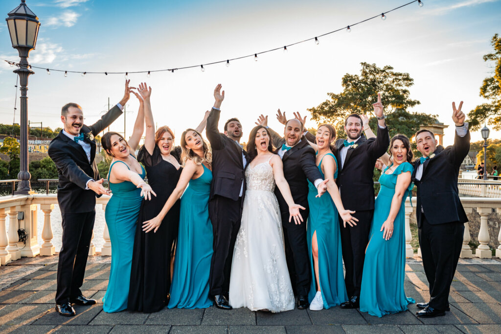 The happy couple strikes a pose with their awesome bridesmaids and groomsmen on a gorgeous lakeside patio.