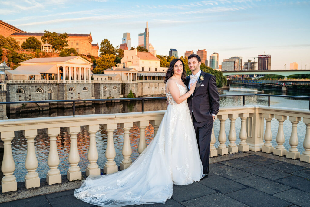 Newlywed couple, glowing with happiness, pose for a photo on a picturesque lakeside terrace.