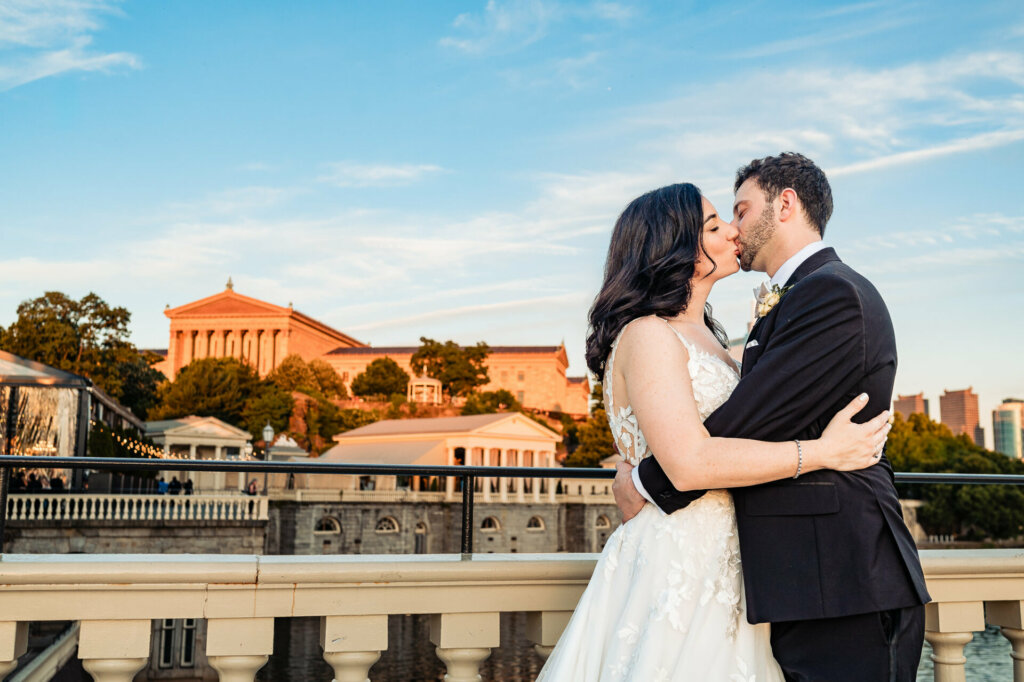 Blissful newlyweds, locked in a kiss on a scenic lakeside terrace.