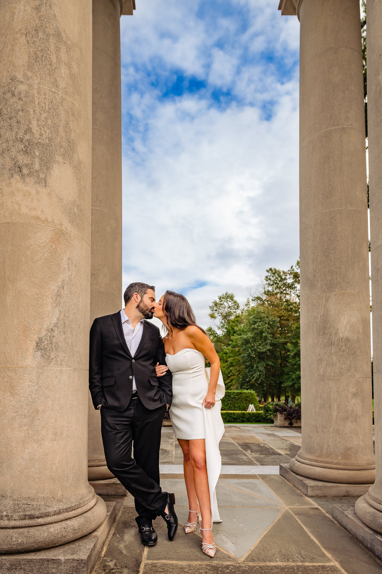 The woman leans in for a kiss from her partner while they pose together during their engagement session.