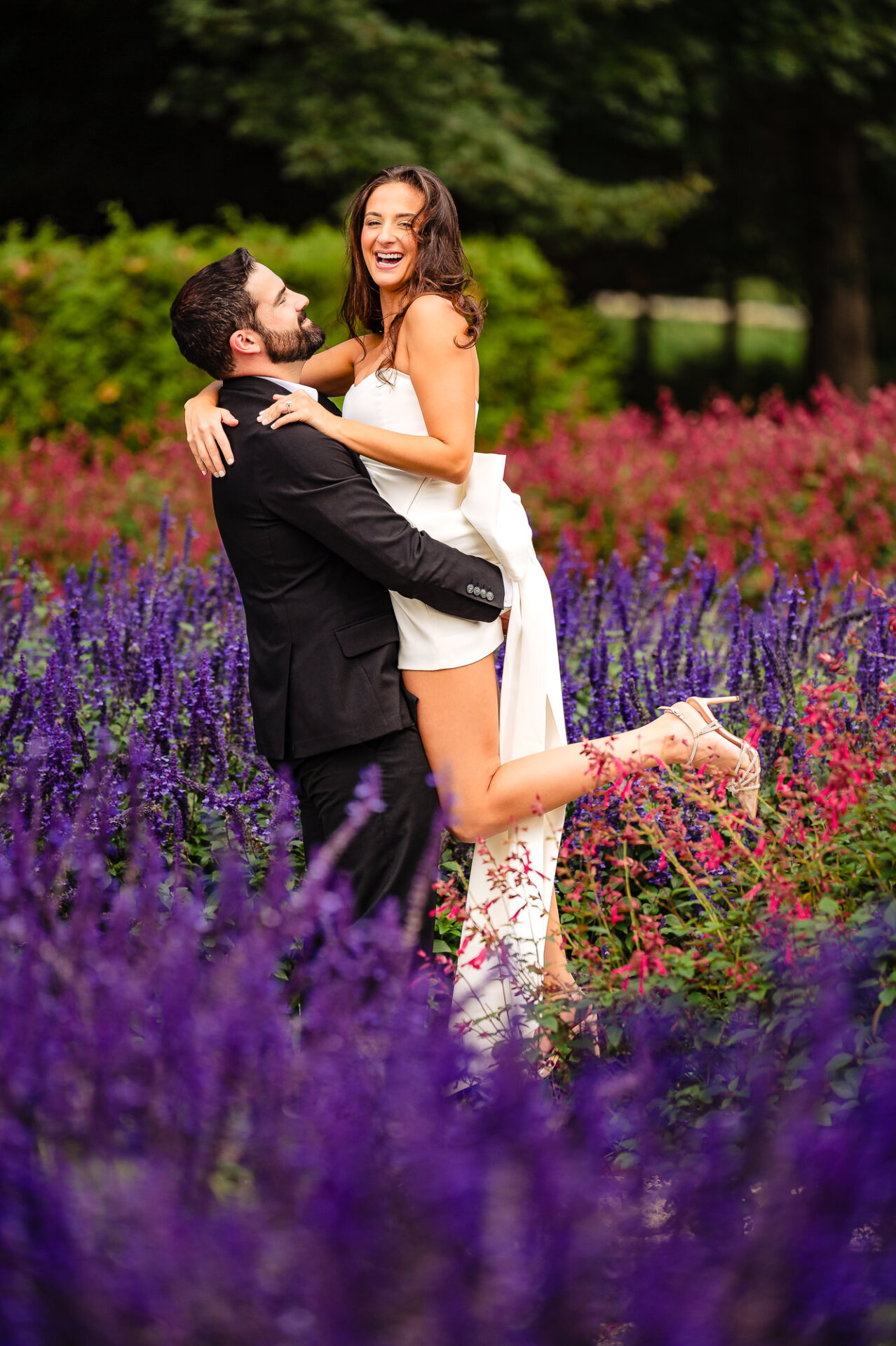 A couple stands in the garden at Nemours Estate, smiling and looking at each other during their engagement photoshoot.