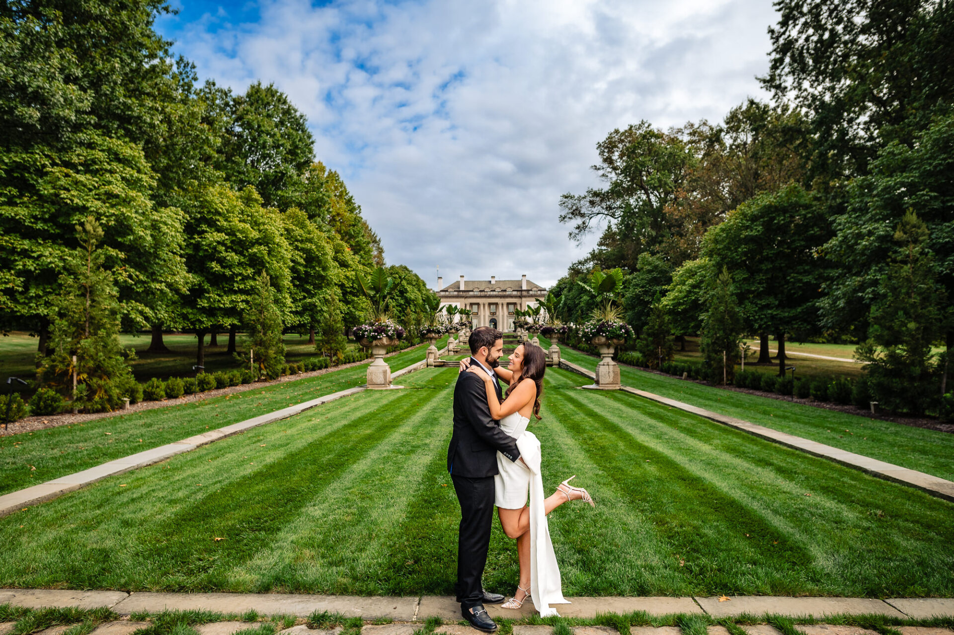The couple smiles affectionately at each other while posing in the lush gardens of Nemours Estate during their engagement photoshoot.
