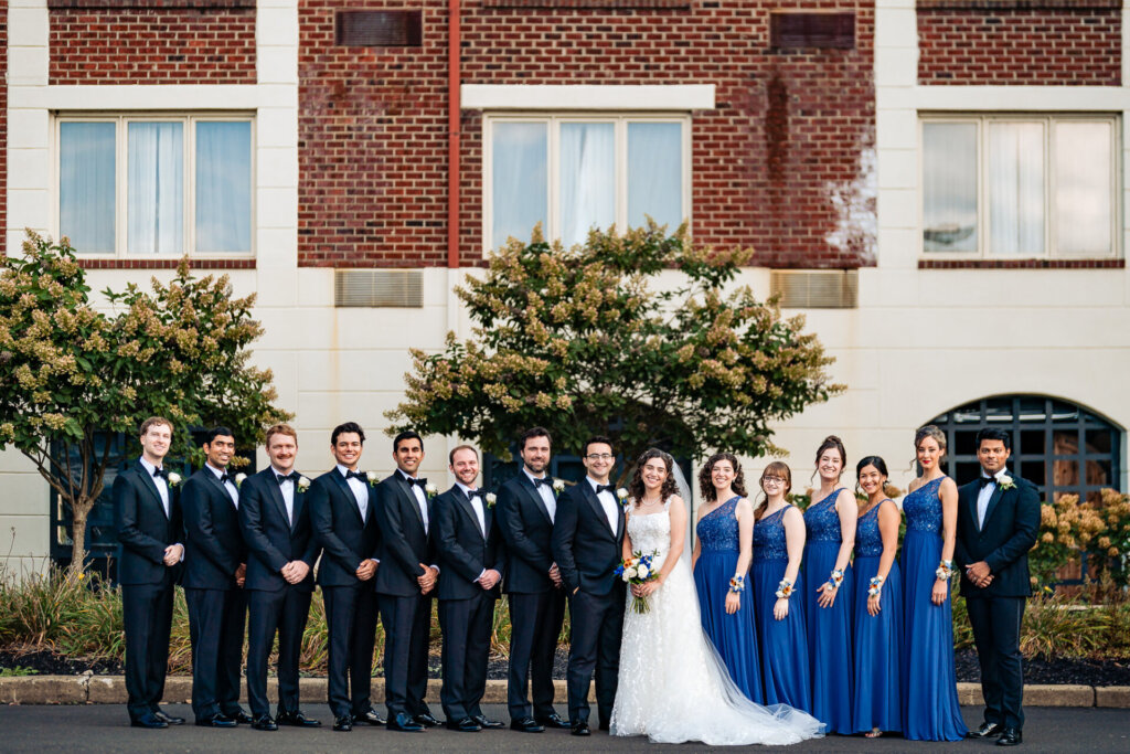 Newlyweds walk alongside their bridesmaids and groomsmen in a formal shot, capturing the elegance and unity of the bridal party.