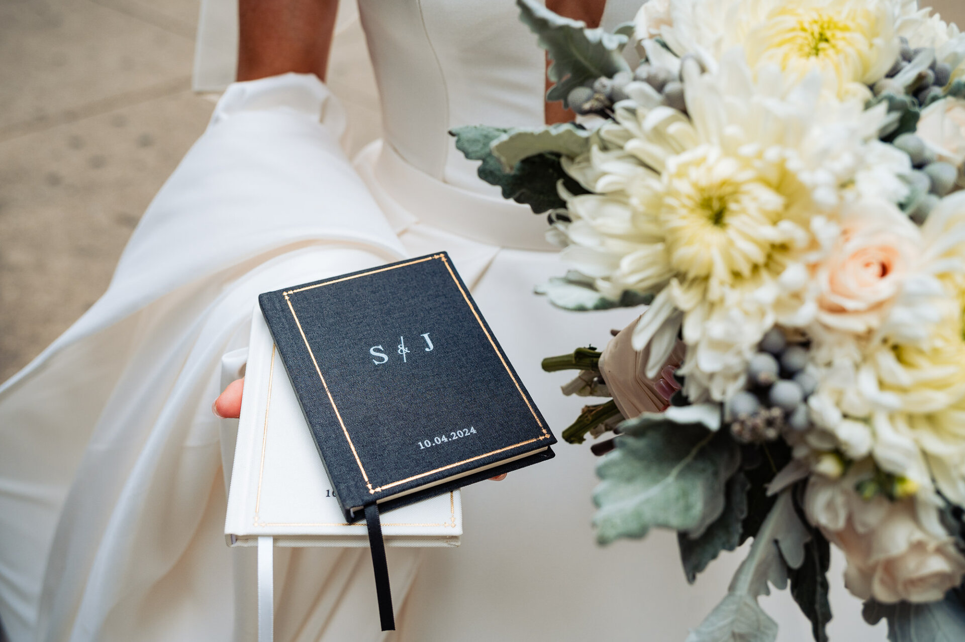 Black and white booklet of the bride and groom resting on the bride's palm, with a bouquet of flowers held in her other hand.