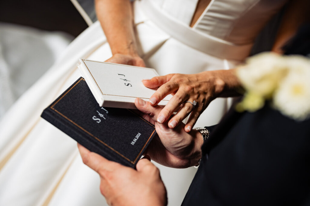 Close-up of the bride and groom holding a small black and white booklet with their initials elegantly displayed on the cover.