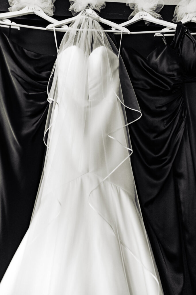 A white wedding gown displayed in front of black bridesmaids' dresses, creating a striking contrast against a neutral backdrop.