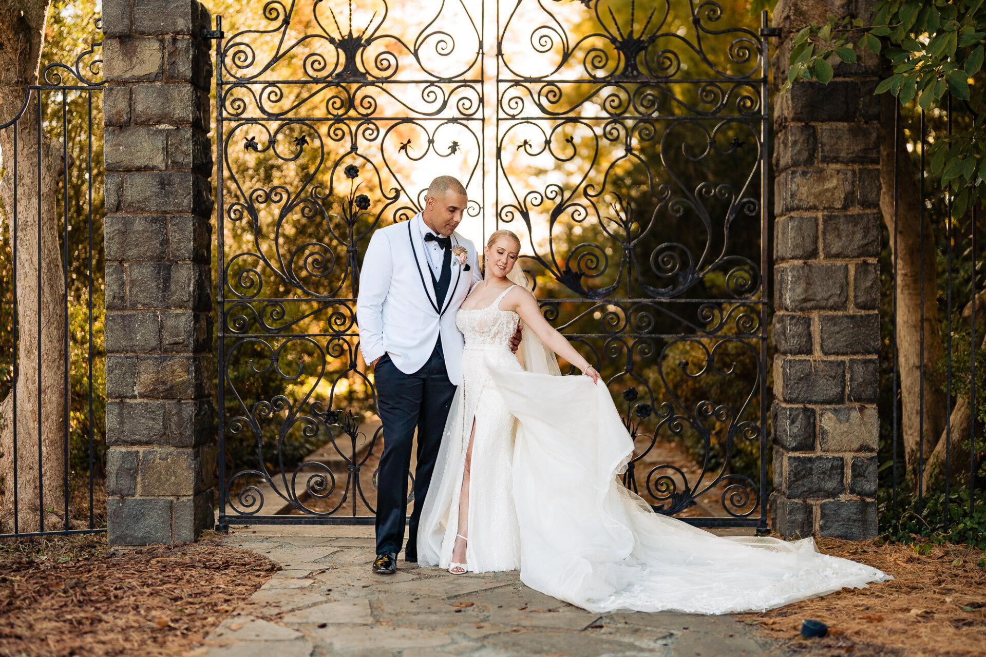 Bride and groom holding hands and smiling at each other while standing near a historic iron gate in a garden setting