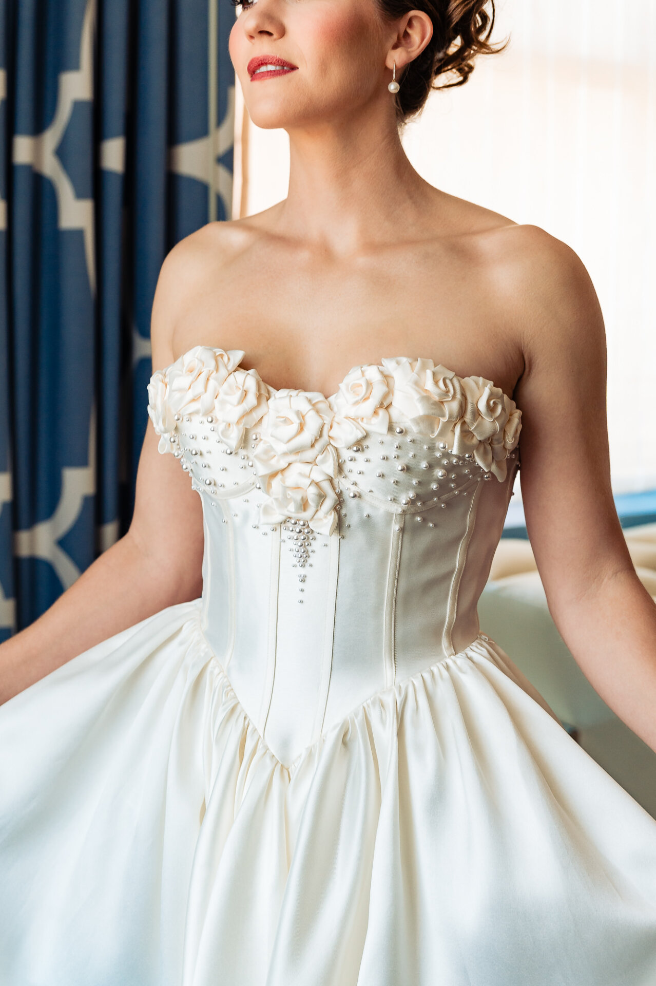 Close-up of the bride’s upper body, focusing on the intricate floral appliqué and beaded details of the wedding gown's bodice. Soft natural light highlights the delicate texture of the dress.