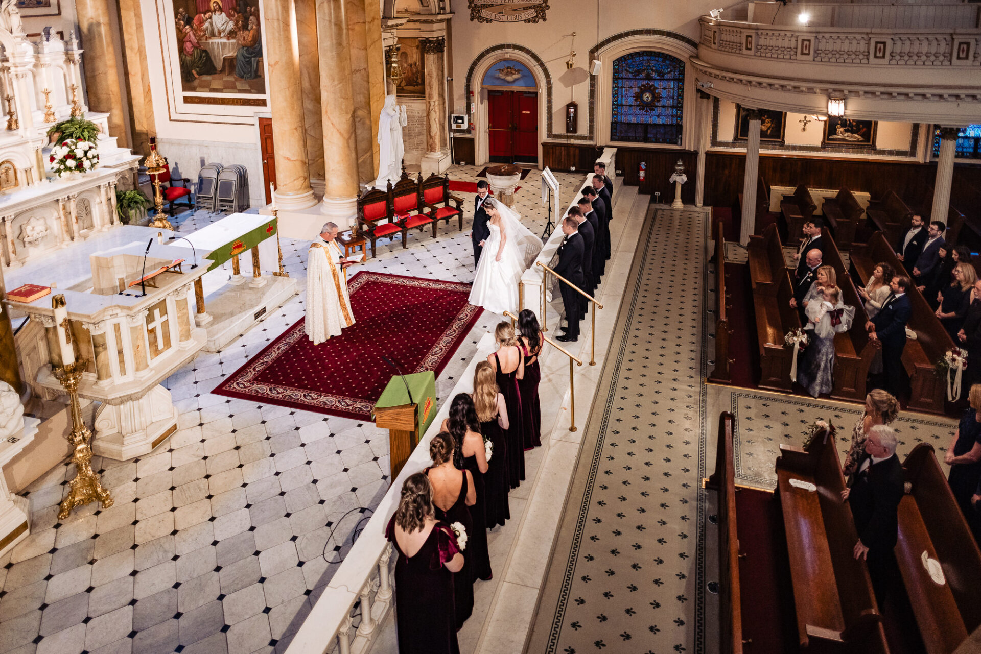 Elevated side angle showing the bride and groom at the altar, with the aisle and floral decorations in the background.