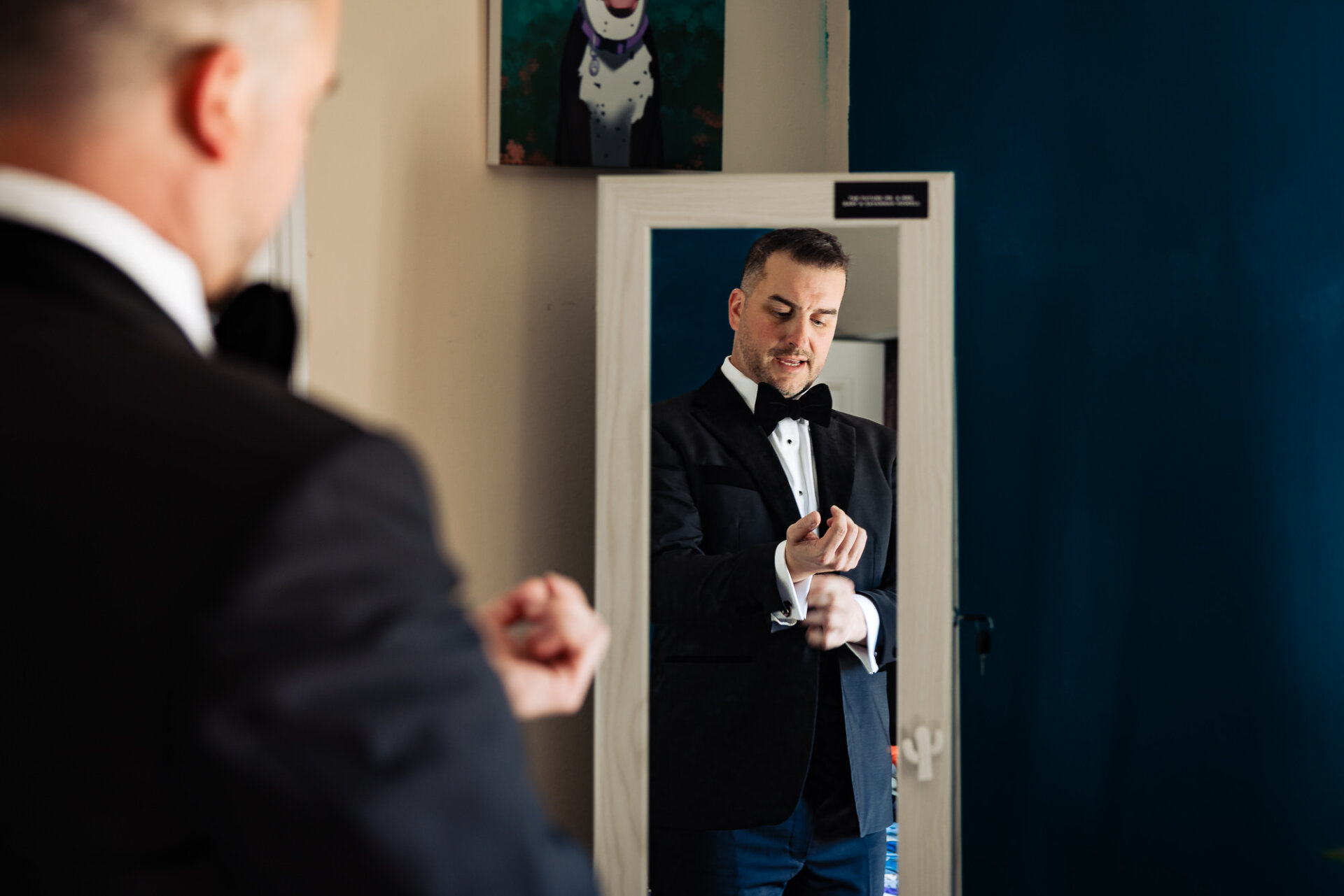 Groom in his wedding suit adjusting his cufflinks while standing in front of a mirror.