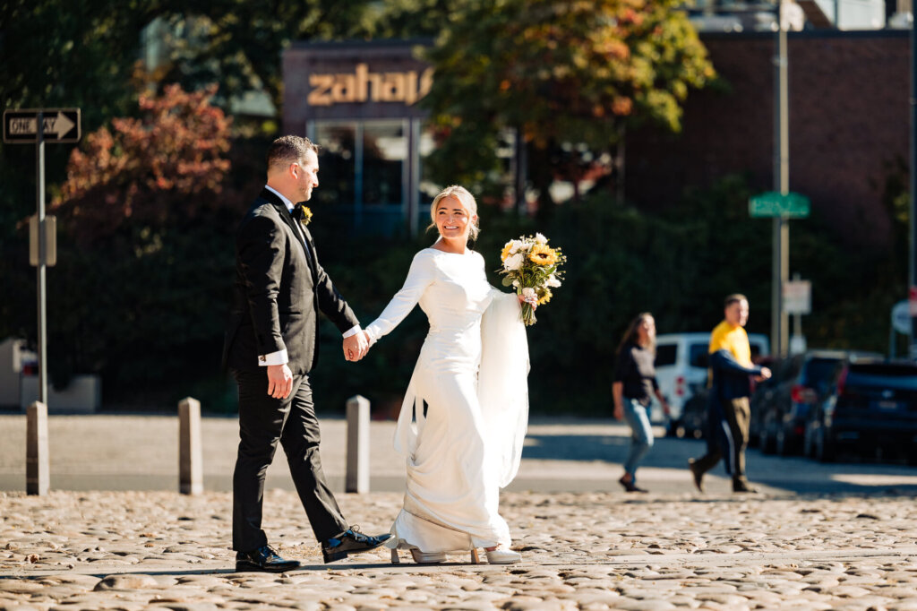 Bride and groom walking through a vibrant street with a bouquet in the bride's hand and a warm sunlight.