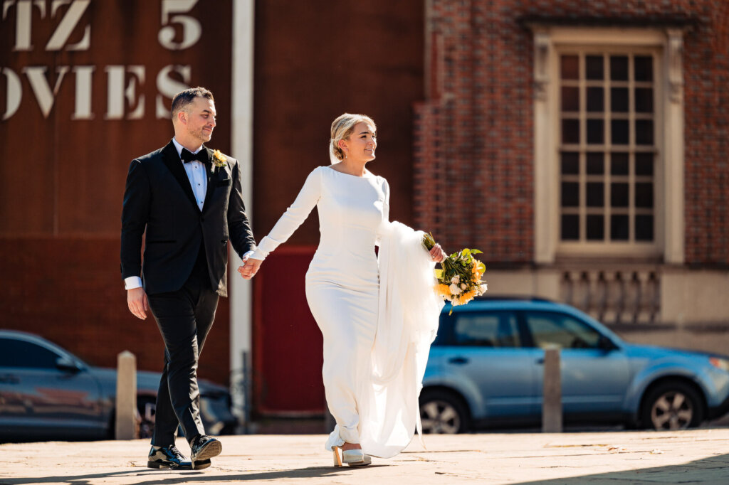 Bride and groom walking hand in hand down a cobblestone street, enjoying a joyful moment together.