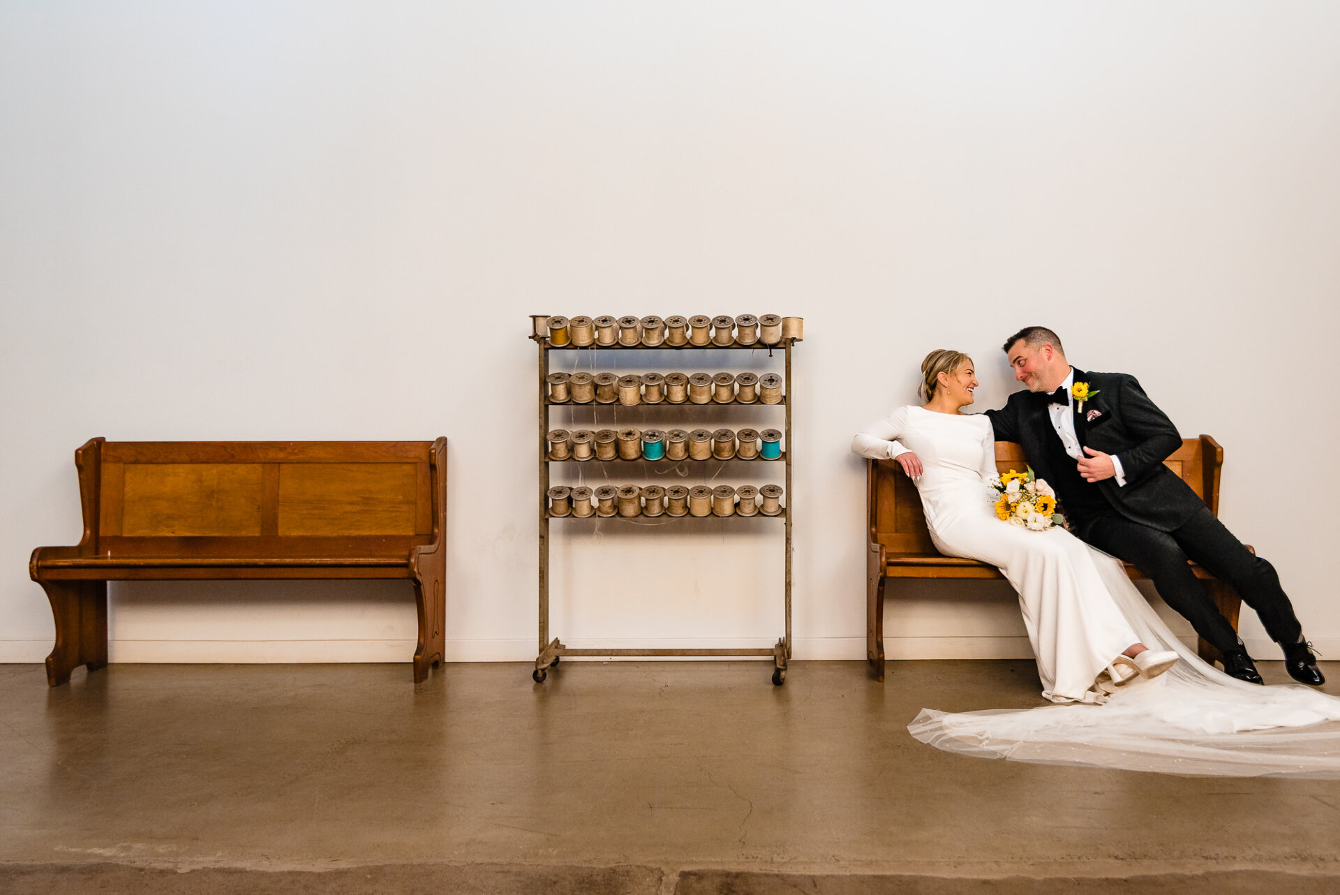 Bride leaning back on a bench with the groom beside her, both sharing a relaxed and playful moment.