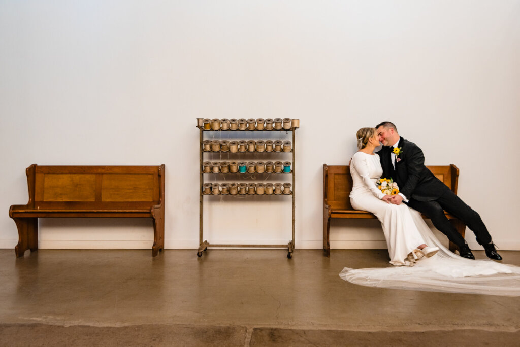 Bride leaning back on a bench with the groom beside her, both smiling and enjoying a relaxed, playful moment.