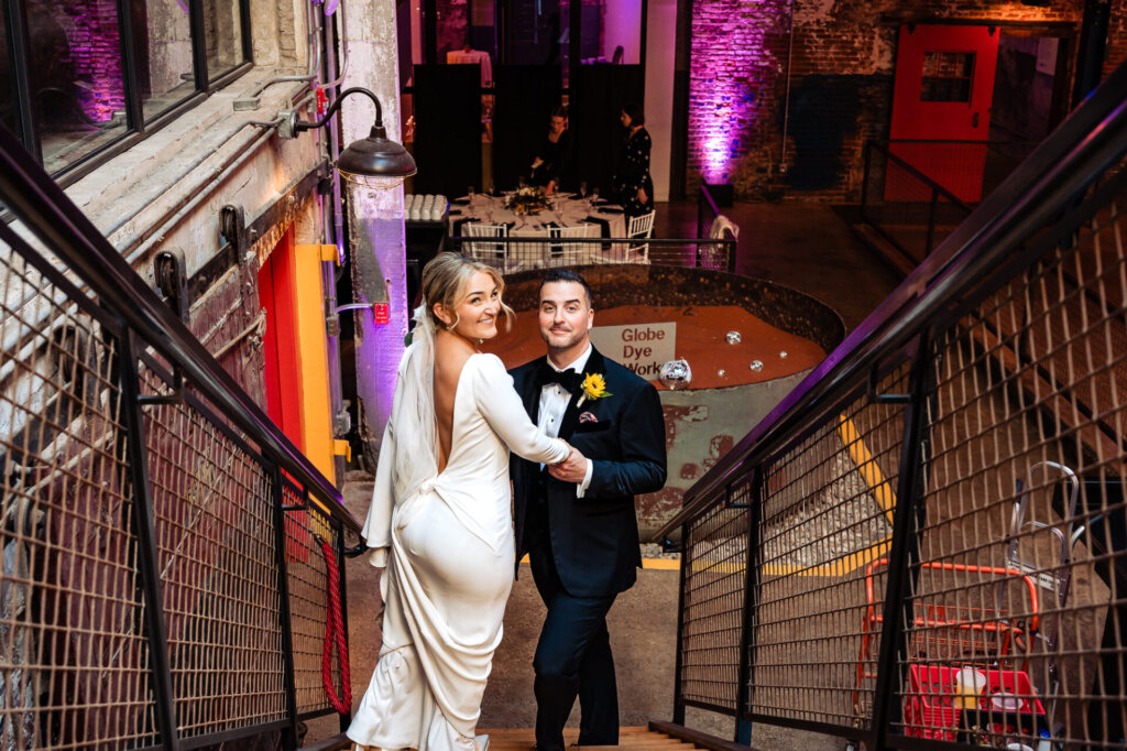 Bride and groom walking down a staircase together, smiling and holding hands as they enter the reception