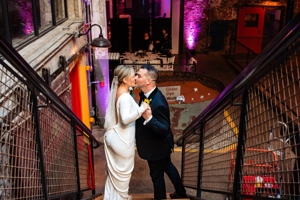Bride and groom walking hand-in-hand down a staircase kissing