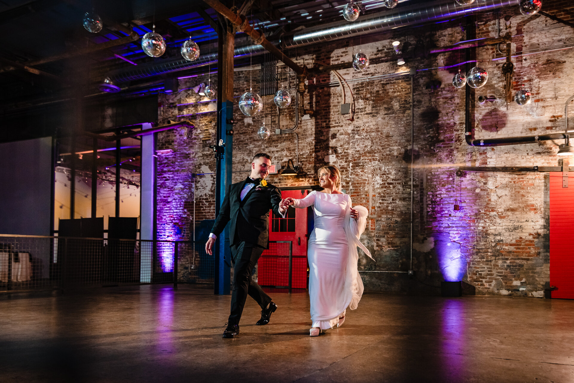 Bride and groom dancing joyfully on the dance floor at their wedding reception, with colorful lighting in the background