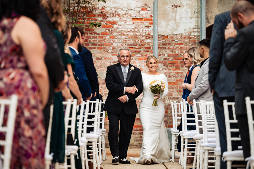 Bride walking down the aisle with her father as guests stand to witness the ceremony